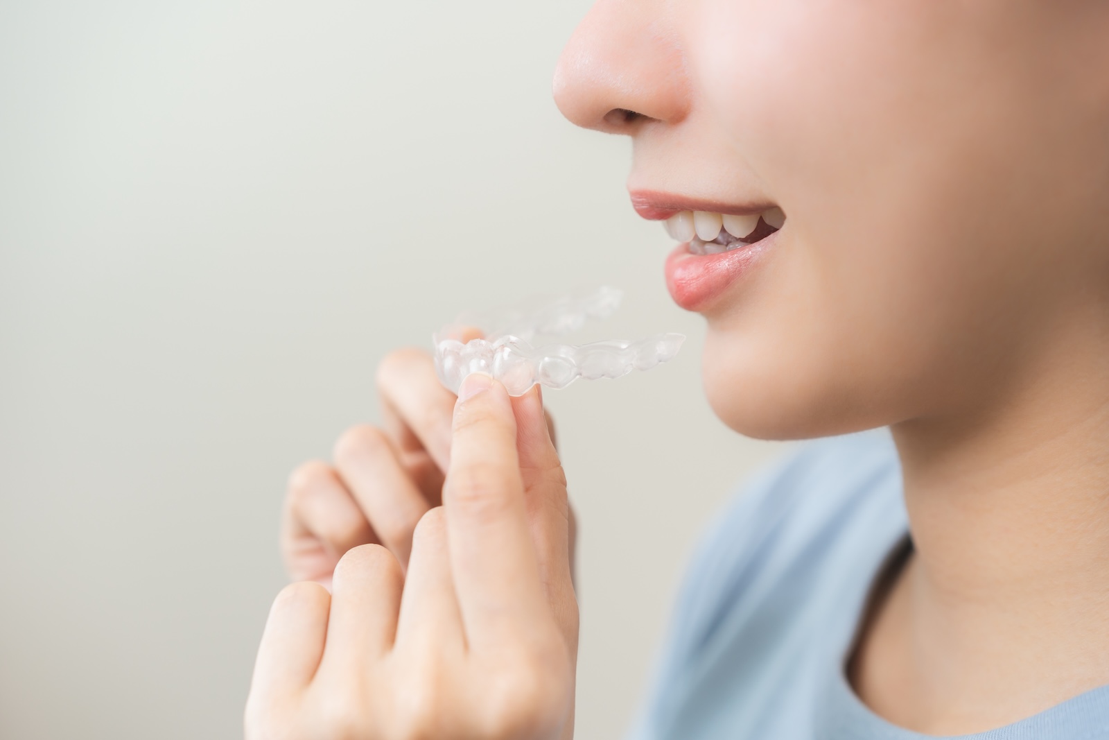  A woman holds a clear aligner up to her lips, ready to try on her aligner.
