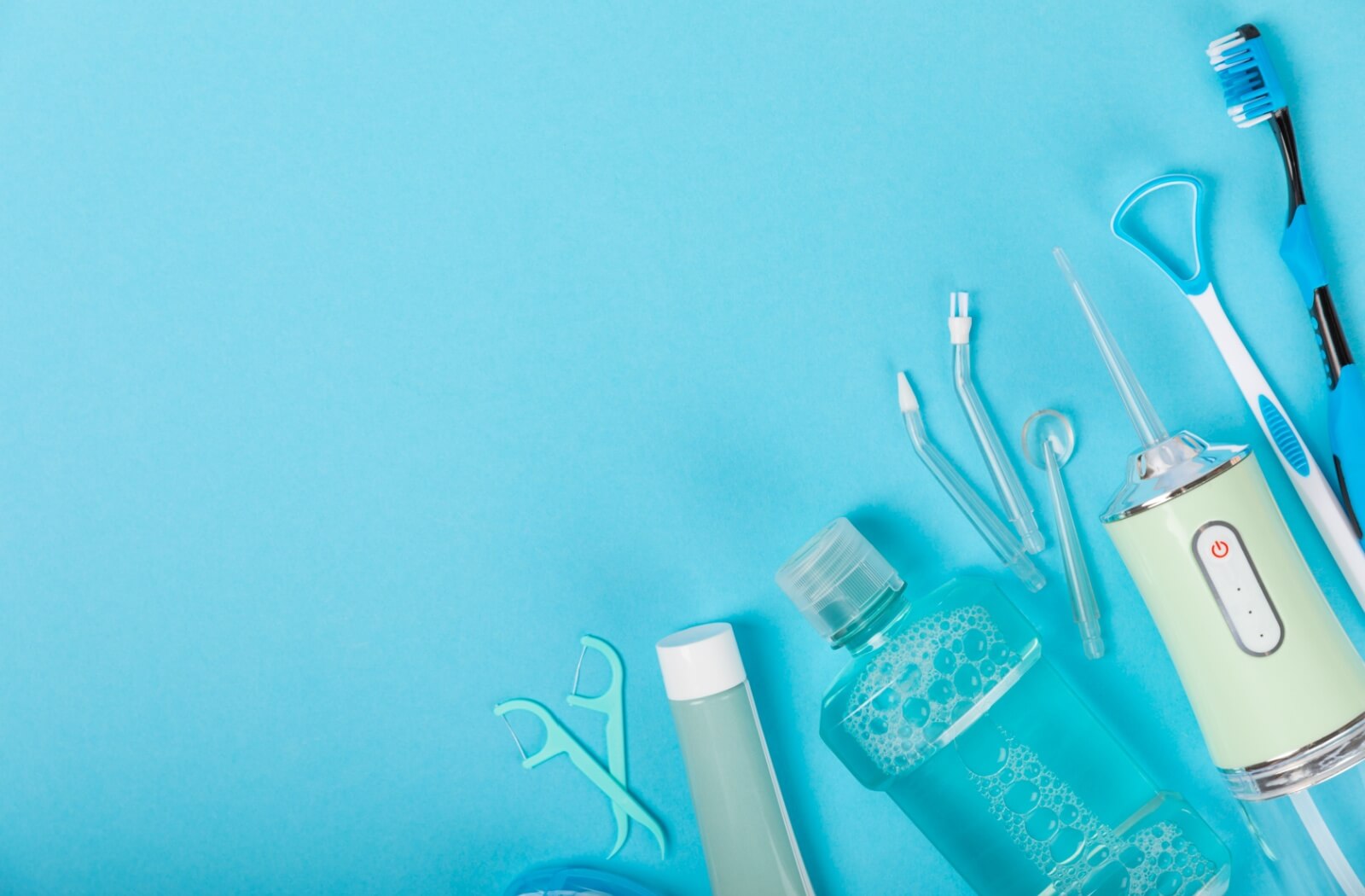 Many oral cleaning devices for home lay arranged on a counter. Included are floss picks, mouthwash, a water flosser, a tongue cleaner and, a toothbrush.