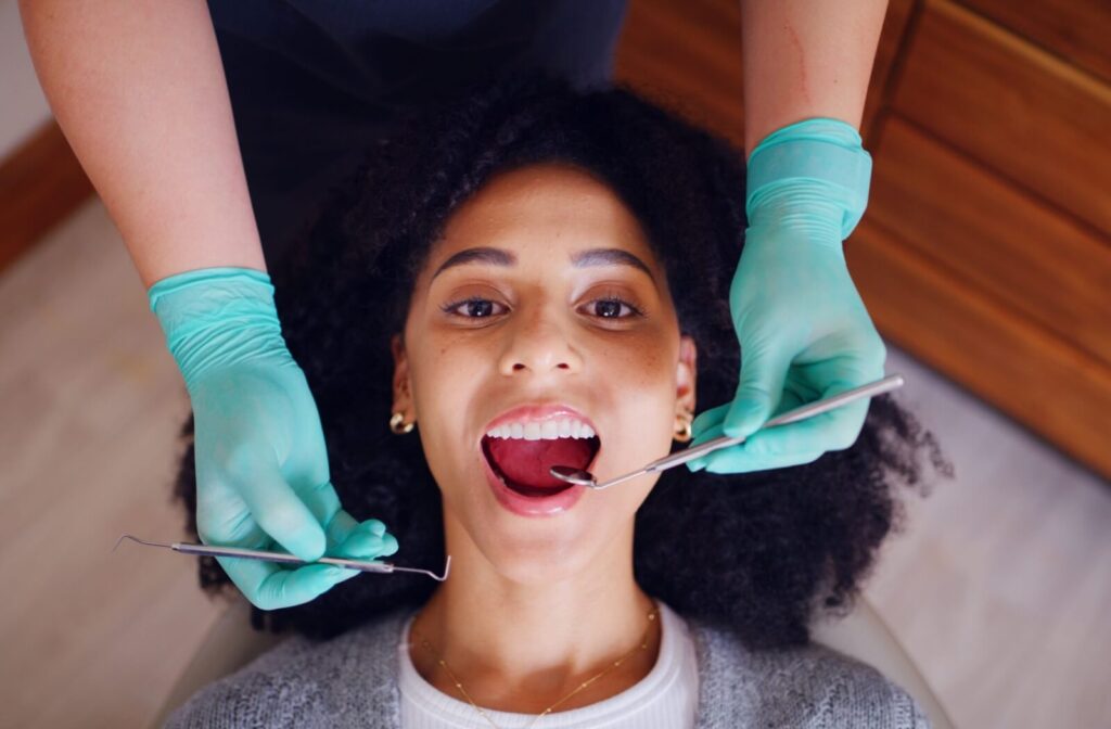 A dental patient looking up at the camera with their mouth open while a provider in teal gloves uses dental tools for an exam.